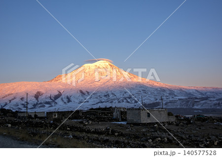 Majestic snow-capped Mount Ararat (Agri Dagi) at golden hour sunrise with a small rural village in the foreground, Turkey. Majestic snow-capped Mount Ararat (Agri Dagi) at golden hour sunrise with a small rural village in the foreground, Turkey. 140577528