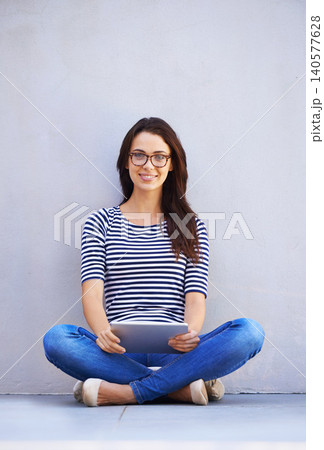 Portrait, smile and tablet for social media with woman on wall background for internet research. App, email and technology with happy young person legs crossed on floor for online information 140577628