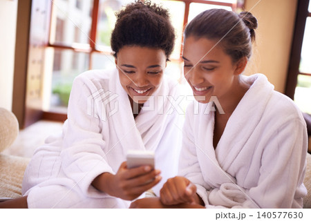 Beauty, phone and spa with woman friends in robes for luxury pampering or treatment together. Smile, app and social media with happy young people at resort or salon for wellness or weekend getaway 140577630