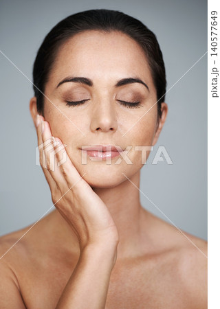 Beauty, mature and skincare of woman touching face with makeup at studio isolated on gray background. Cosmetics, glow and hand of model in facial treatment for dermatology, anti aging and eyes closed 140577649