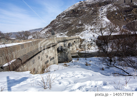 Historical Stone Bridge in Kars covered in snow framed by an old tree in winter, Turkey 140577667