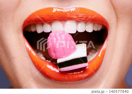Beauty, lipstick and woman with sweets in mouth, makeup and creativity with closeup of shiny cosmetic product. Licorice, candy and orange lip gloss for aesthetic, art and cosmetology with glamour Beauty, lipstick and woman with sweets in mouth, makeup and creativity with closeup of shiny cosmetic product. Licorice, candy and orange lip gloss for aesthetic, art and cosmetology with glamour 140577840