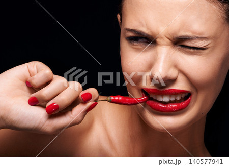 Beauty, makeup and woman eating chilli in studio with manicure on hand isolated on a black background. Cosmetics, model and person with pepper in mouth, food or healthy vegetable for skincare on face 140577941