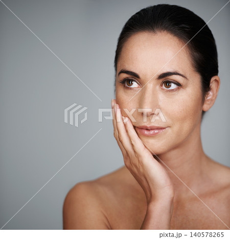 Beauty, skincare and woman touching face in makeup at studio isolated on a gray background mockup. Cosmetics, hand and model in facial treatment for dermatology, thinking and health for anti aging Beauty, skincare and woman touching face in makeup at studio isolated on a gray background mockup. Cosmetics, hand and model in facial treatment for dermatology, thinking and health for anti aging 140578265
