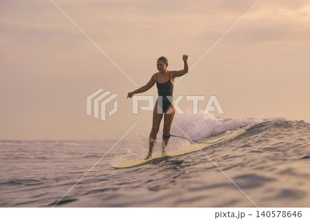 Woman Surfs Sunset, Sunset Illuminates Ocean As Woman Surfs Closer 140578646