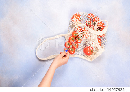 Hand holding cherry tomatoes from reusable mesh bag Hand holding cherry tomatoes from reusable mesh bag 140579234