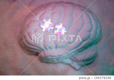 White brain-shaped sculpture with two colorful puzzle pieces resting on top, set against a soft, textured background with subtle lighting effects 140579298