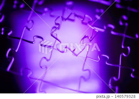 Close-up of interlocking puzzle pieces illuminated by purple light, showcasing intricate details and textures of the jigsaw puzzle against a blurred background 140579328