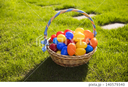 Colorful plastic Easter eggs in a woven basket resting on green grass under bright sunlight, perfect for spring celebrations and holiday activities Colorful plastic Easter eggs in a woven basket resting on green grass under bright sunlight, perfect for spring celebrations and holiday activities 140579340