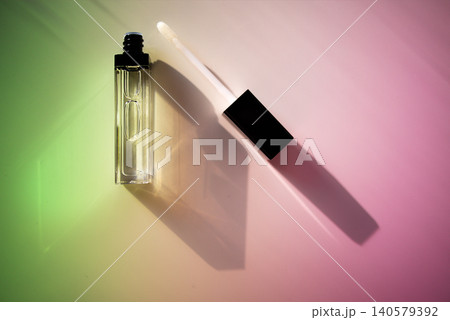 Clear gloss lips bottle with black cap and applicator lying on a colorful gradient background, showcasing beauty product packaging design Clear gloss lips bottle with black cap and applicator lying on a colorful gradient background, showcasing beauty product packaging design 140579392