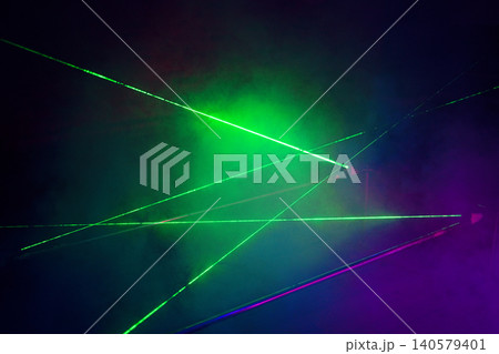 Colorful laser beams in green and purple hues create dynamic patterns against a dark background with smoke effects enhancing the visual impact of the scene Colorful laser beams in green and purple hues create dynamic patterns against a dark background with smoke effects enhancing the visual impact of the scene 140579401
