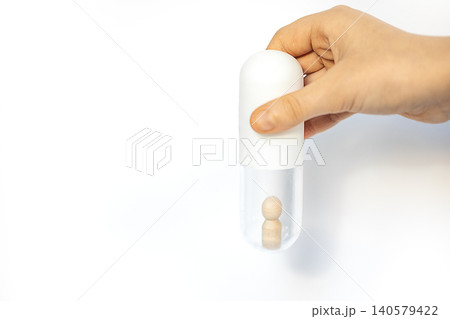 Hand holding a transparent capsule with a wooden figure inside, showcasing a unique design concept for health, wellness, or medication packaging Hand holding a transparent capsule with a wooden figure inside, showcasing a unique design concept for health, wellness, or medication packaging 140579422