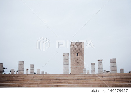 Historic stone columns surround a tall ancient tower under a cloudy sky, creating a serene atmosphere in a historical site with architectural significance and cultural heritage 140579437