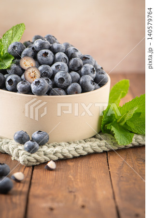 A side angle shot of a ceramic bowl filled with ripe blueberries, garnished with fresh mint leaves on a textured placemat and a rustic wooden surface A side angle shot of a ceramic bowl filled with ripe blueberries, garnished with fresh mint leaves on a textured placemat and a rustic wooden surface 140579764