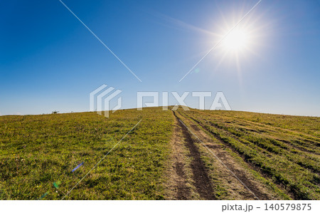 A large grassy area stretches out under a clear blue sky with the sun shining brightly 140579875