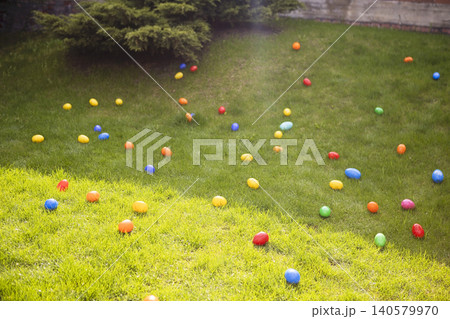 Colorful plastic Easter eggs scattered across a green lawn in a backyard setting, surrounded by shrubs and trees under bright sunlight Colorful plastic Easter eggs scattered across a green lawn in a backyard setting, surrounded by shrubs and trees under bright sunlight 140579970