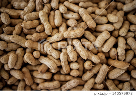 Raw, unprocessed peanuts in their shells scattered on a surface, showcasing their natural brown color and texture, ideal for culinary and agricultural contexts 140579978