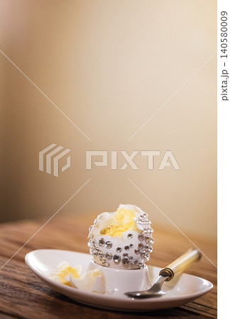 Decorative dessert with whipped cream and silver embellishments served on a white plate, accompanied by a small spoon on a wooden table 140580009