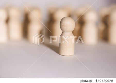 Wooden figurine standing alone in focus with blurred background of similar figures, representing individuality and uniqueness in a minimalist setting Wooden figurine standing alone in focus with blurred background of similar figures, representing individuality and uniqueness in a minimalist setting 140580026