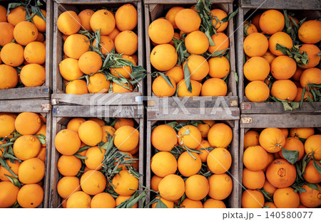 Fresh oranges stacked in wooden crates, showcasing vibrant colors and lush green leaves, highlighting the abundance of citrus fruits in a rustic market setting 140580077