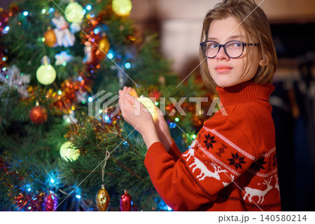 boy in a sweater decorates a new year tree with a glowing garland for new year boy in a sweater decorates a new year tree with a glowing garland for new year 140580214