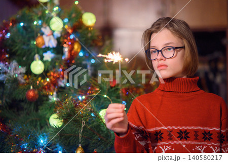 boy in a red sweater holds a burning sparkler next to a decorated christmas tree boy in a red sweater holds a burning sparkler next to a decorated christmas tree 140580217