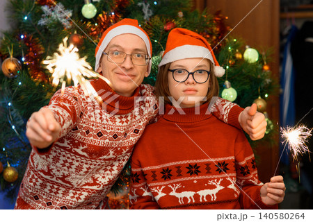 man shows a thumb up and a boy holds a sparkler near a christmas tree man shows a thumb up and a boy holds a sparkler near a christmas tree 140580264