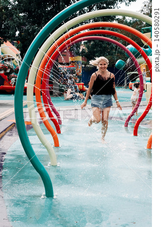 blonde girl running under arches with water splashes at a water playground blonde girl running under arches with water splashes at a water playground 140580291
