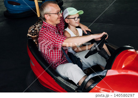 father hugging his son in a red bumper car at an amusement ride 140580297