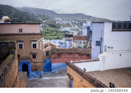 Scenic view of colorful buildings in a hillside village, showcasing traditional architecture with vibrant hues, surrounded by lush greenery and cloudy sky, evoking a serene atmosphere 140580549