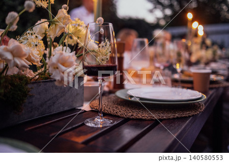 Elegant outdoor dining setup featuring a beautifully arranged table with floral centerpieces, wine glasses, and plates, creating a warm and inviting atmosphere for gatherings Elegant outdoor dining setup featuring a beautifully arranged table with floral centerpieces, wine glasses, and plates, creating a warm and inviting atmosphere for gatherings 140580553