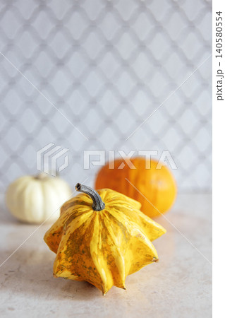 Unique yellow gourd with ridged texture is placed in front of white and orange pumpkins on a light surface, creating a vibrant autumnal display with seasonal charm 140580554
