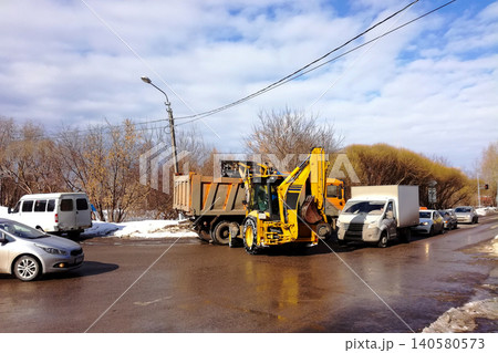 yellow loader clears the city road of snow next to a truck in a traffic jam yellow loader clears the city road of snow next to a truck in a traffic jam 140580573