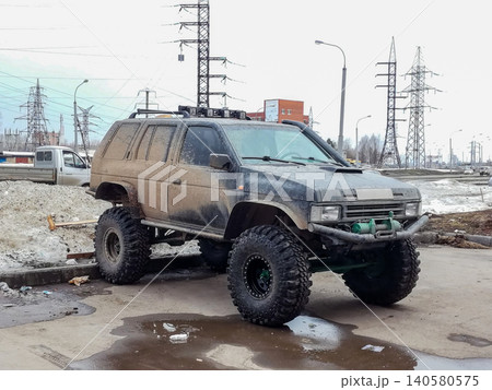 black dirty SUV on large embossed wheels stands on asphalt near a puddle black dirty SUV on large embossed wheels stands on asphalt near a puddle 140580575