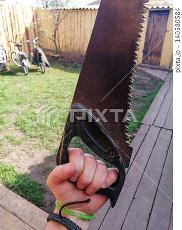 men hand tightly holds an old rusty hand saw for wood in the yard outdoors men hand tightly holds an old rusty hand saw for wood in the yard outdoors 140580584