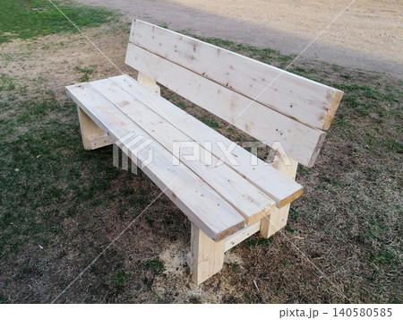 new empty wooden bench with a backrest installed on green grass near a dirt road 140580585