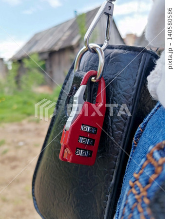 red combination lock with three digits is fixed on the carabiner of a black leather bag close up 140580586