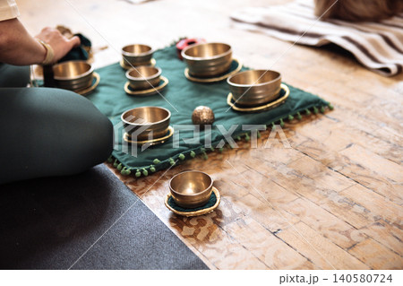 Individual practicing mindfulness with brass singing bowls arranged on a green cloth mat, creating a serene atmosphere for meditation and relaxation in a tranquil environment 140580724