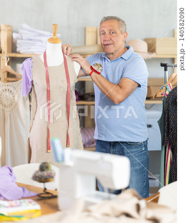 Mature man tailor connects parts of dress on mannequin Mature man tailor connects parts of dress on mannequin 140582090