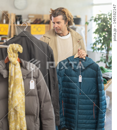 man chooses between a raincoat and a down jacket 140582147