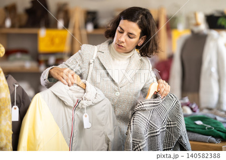 Latin American woman search and choose coat or jacket in shop, compare goods Latin American woman search and choose coat or jacket in shop, compare goods 140582388
