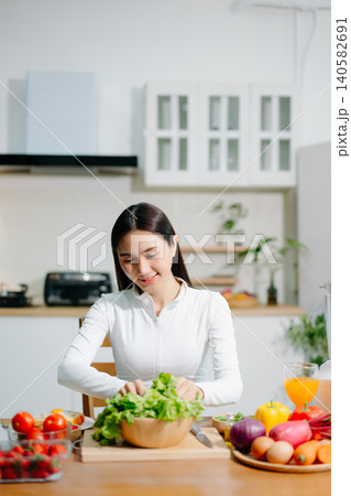 Healthy woman cooking fresh vegetables at home kitchen while using tablet. Clean eating, nutrition, meal prep, healthy lifestyle and modern cooking concept. 140582691