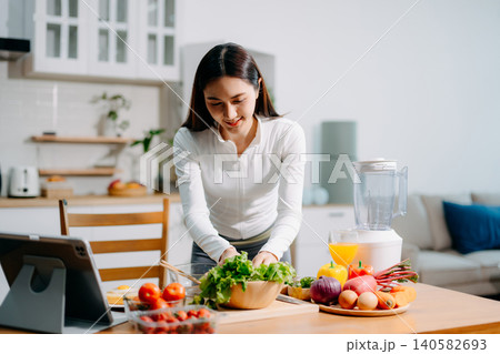 Asian woman preparing fresh salad, reflecting healthy lifestyle, clean eating, nutrition, organic vegetables, and modern home kitchen environment. Asian woman preparing fresh salad, reflecting healthy lifestyle, clean eating, nutrition, organic vegetables, and modern home kitchen environment. 140582693