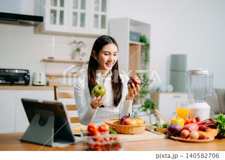 Smiling young woman preparing fresh strawberries, fruit and vegetables in a modern kitchen. Healthy lifestyle, clean eating, vegan nutrition and home cooking concept. 140582706