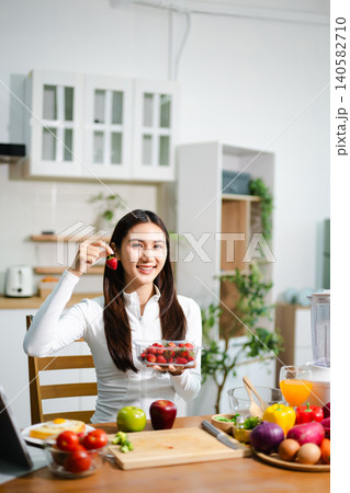 Young woman preparing fresh tomatoes and vegetables in modern kitchen. Healthy cooking, smoothie blender, clean eating, vegan lifestyle and online food blog concept. Young woman preparing fresh tomatoes and vegetables in modern kitchen. Healthy cooking, smoothie blender, clean eating, vegan lifestyle and online food blog concept. 140582710