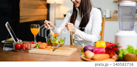Young woman eating fresh salad in modern kitchen while using tablet. Healthy food, diet lifestyle, online cooking tutorial, wellness and clean eating concept. Young woman eating fresh salad in modern kitchen while using tablet. Healthy food, diet lifestyle, online cooking tutorial, wellness and clean eating concept. 140582716