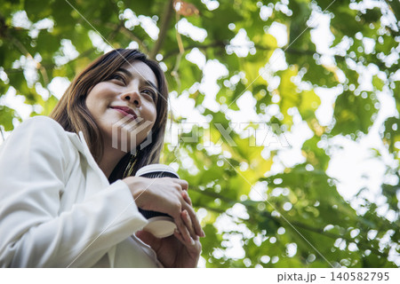 Woman drinking coffee hands holding hot disposable cup in green park. Happy Relax beautiful asian woman smiling face standing outdoors garden. Young women enjoy nature morning Freedom Lifestyle. Woman drinking coffee hands holding hot disposable cup in green park. Happy Relax beautiful asian woman smiling face standing outdoors garden. Young women enjoy nature morning Freedom Lifestyle. 140582795