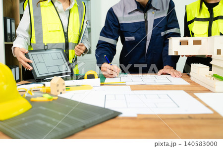 Engineers and architects reviewing digital blueprint on tablet with tools and plans on desk, representing construction planning, teamwork, engineering design Engineers and architects reviewing digital blueprint on tablet with tools and plans on desk, representing construction planning, teamwork, engineering design 140583000