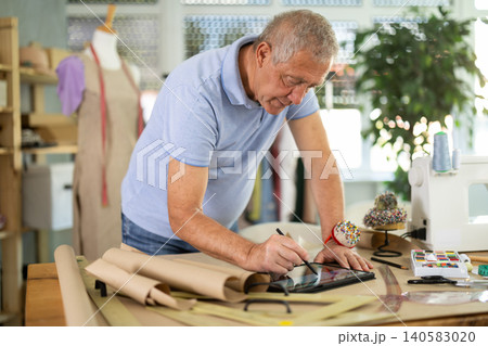 Mature man drawing on tablet in sewing salon Mature man drawing on tablet in sewing salon 140583020