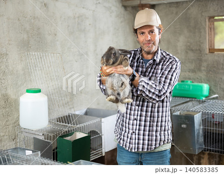 Man farmer with rabbit in her hands on her farm. Farmer takes care of animals Man farmer with rabbit in her hands on her farm. Farmer takes care of animals 140583385